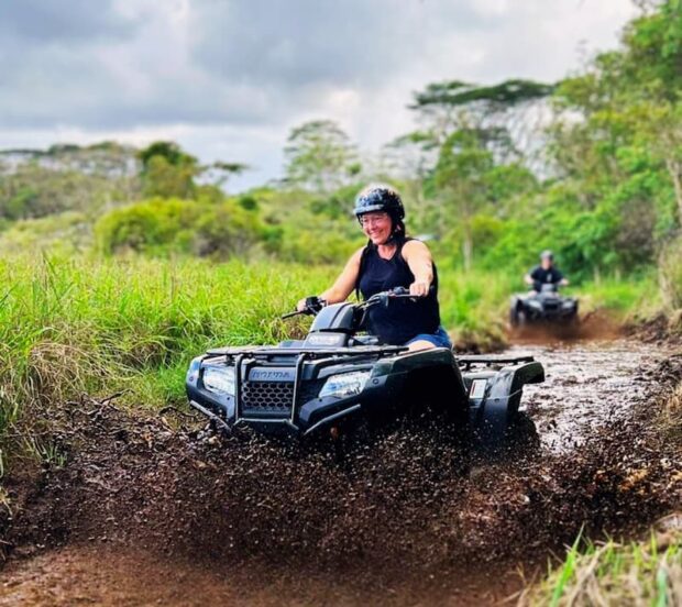 Girl on ATV splashing through a mud puddle on the Ohana Ranch ATV trail, Mountain View Big Island