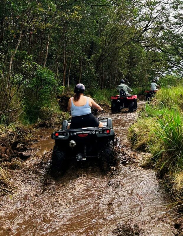Three ATVs riding the farm trail in sequence, last rider emerging from a mud puddle, Ohana Ranch Big Island