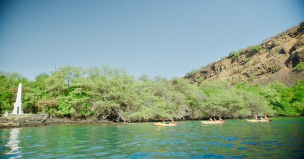 Three tandem kayaks with families pulled up at Kaʻawaloa near the Captain Cook monument