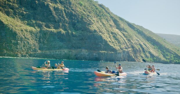 Two kayaks with families on the glassy early-morning water of Kealakekua Bay