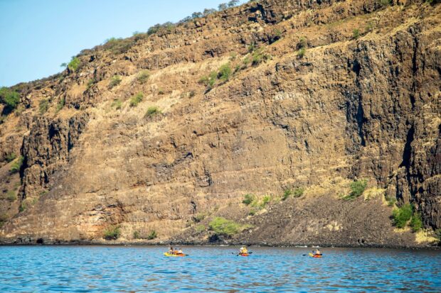Three kayaks with families paddling below the cliffs (pali) of Kealakekua Bay