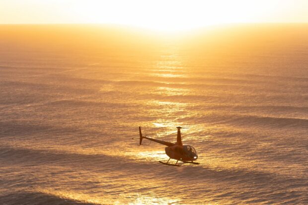 helicopter flying over the ocean during sunset
