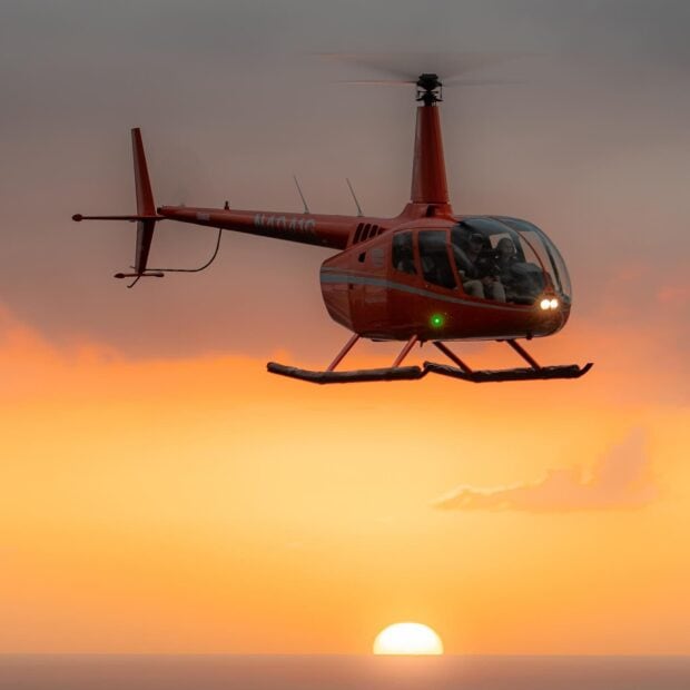 helicopter flying over the ocean during sunset