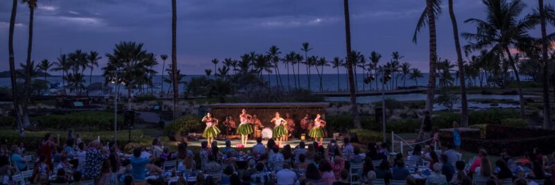 Lit performance stage with front row seating at the Sunset Luau, Waikoloa Beach Marriott, palm trees and ocean at dusk