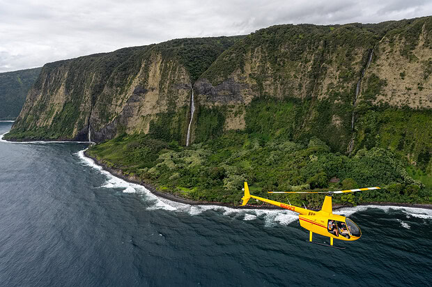 yellow helicopter flying past lush and verdant tropical valleys