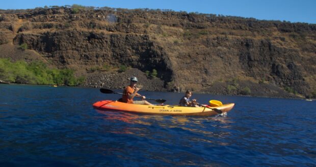 A parent and child throwing a shaka from their kayak on Kealakekua Bay