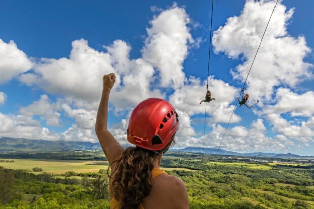 View from below the FlyLine platform at Nui Kauai: a guide cheers as two guests launch on the 400-foot drop in superman pose