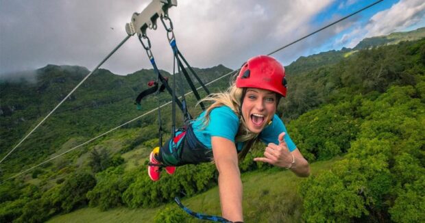 Woman laughing mid-flight on the Powerline zipline at Nui Kauai, superman pose