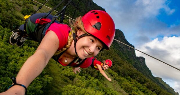 Two women take a selfie mid-flight on the Powerline zipline at Nui Kauai, both in superman pose