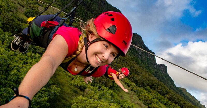 Two women take a selfie mid-flight on the Powerline zipline at Nui Kauai, both in superman pose