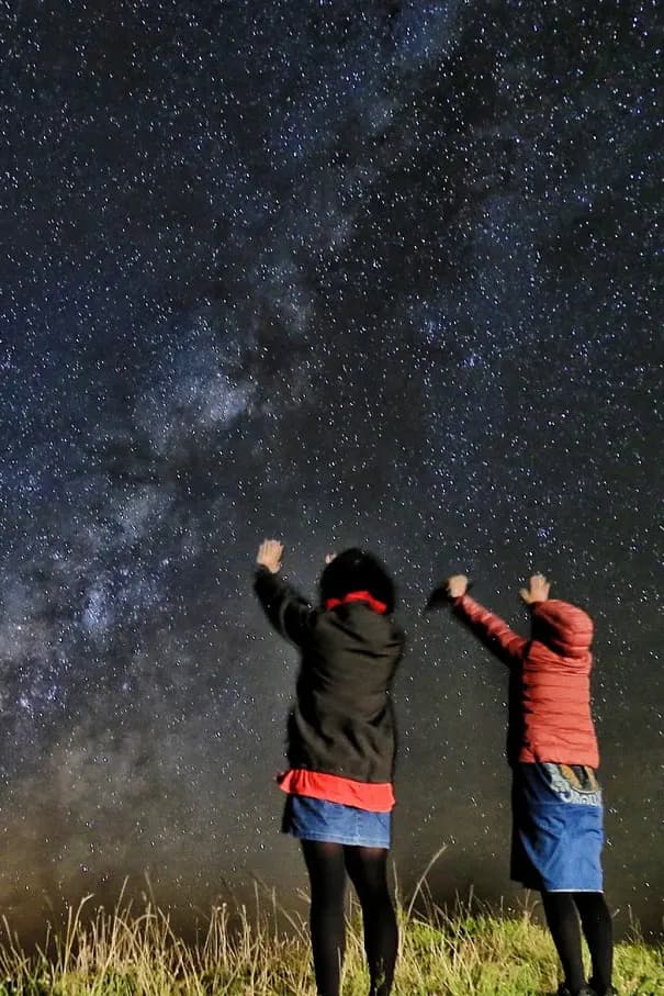 Two tour guests posing under the Milky Way on a long-exposure night photo near Saddle Road