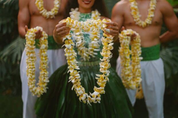 Dancers holding out strands of yellow-and-white plumeria lei at the ʻAhaʻāina Luau