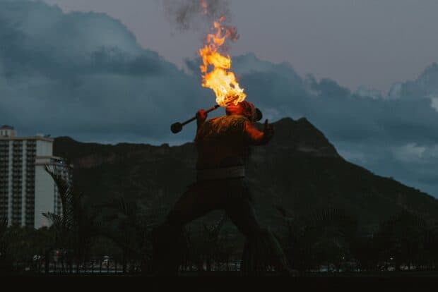 Fire performer with a lit staff silhouetted against Diamond Head at dusk at the ʻAhaʻāina Luau