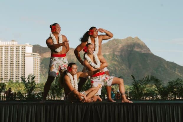 Four male hula dancers posed on the outdoor stage with Diamond Head behind them at ʻAhaʻāina Luau