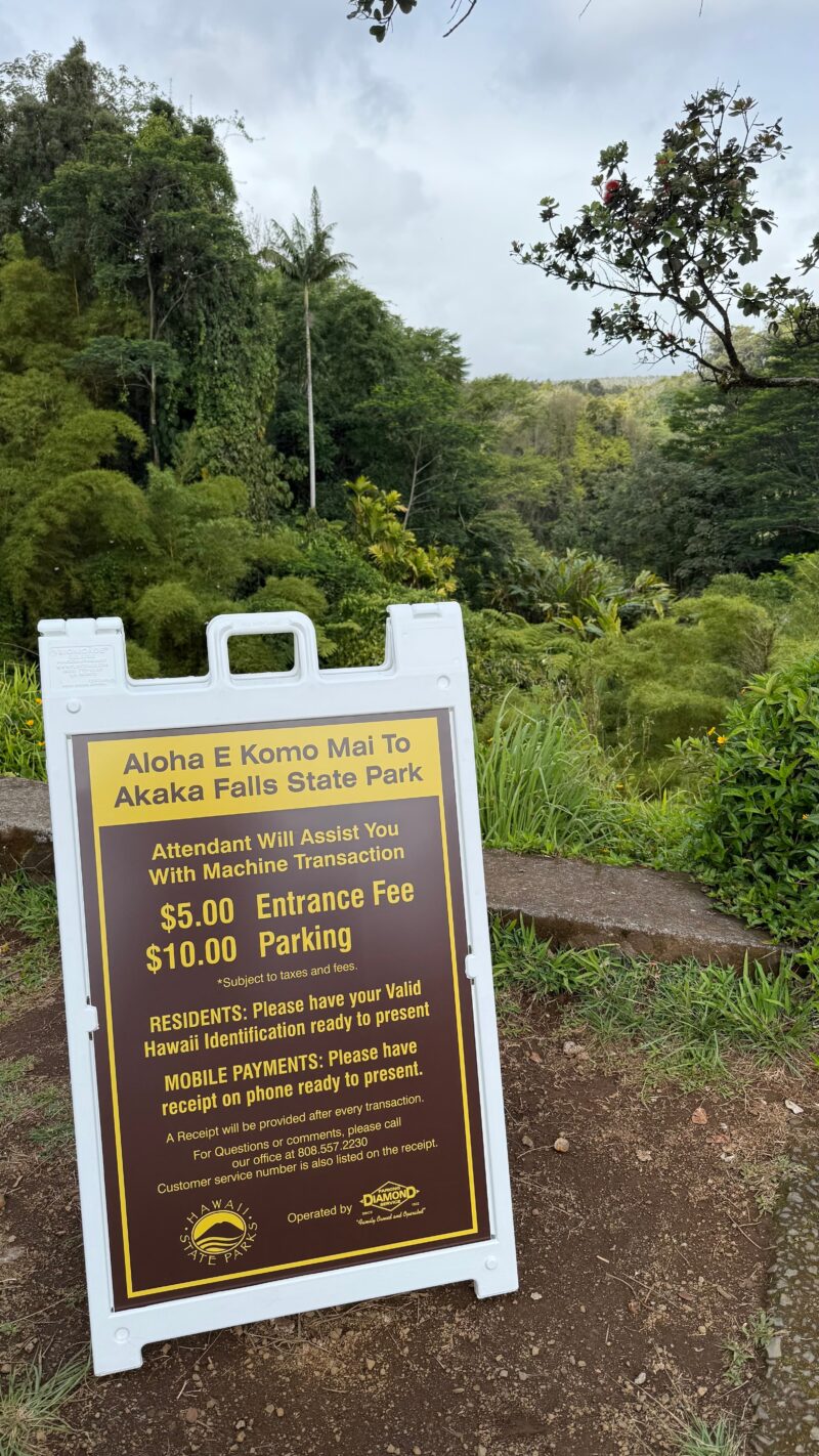 ParkMobile fee sign at the ʻAkaka Falls State Park parking lot listing entrance and parking charges