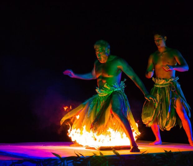 Two male dancers in ti leaf skirts perform beside flames on the stage floor at the Ahi Lele Fire Show, Kauaʻi