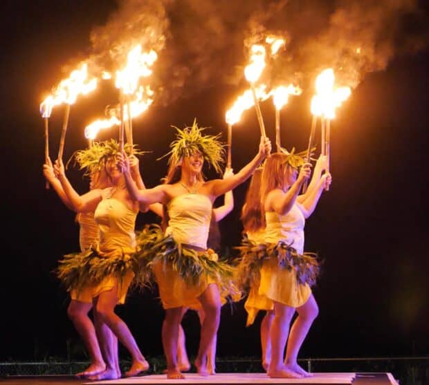 Dancers in ti leaf skirts and headpieces raise flaming torches at the Ahi Lele Fire Show in Kīlauea, Kauaʻi