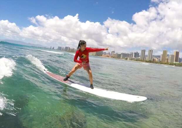 woman standing on longboard for first time at waikiki, oahu, hawaii