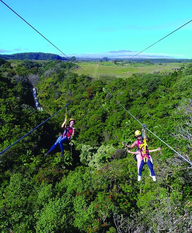 Young child riding tandem with guide on Botanical World Adventures zipline, Big Island