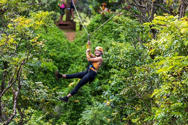 Smiling woman in orange helmet ziplining through the tropical rainforest canopy at Botanical World Adventures, Big Island Hawaii