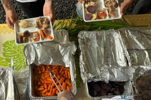Plates of imu-cooked kalua pork, purple sweet potato and carrots above foil trays at the Imu Mea ʻAi food tour