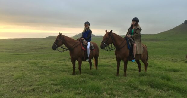 Two riders spread across open pasture in last light, silhouette-style
