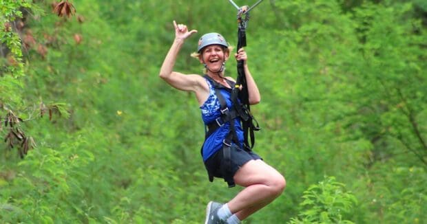 A smiling older woman throws a shaka while ziplining at Coral Crater, Oʻahu