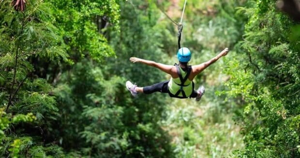 A rider spreads arms and legs while ziplining over green forest at Coral Crater, Oʻahu