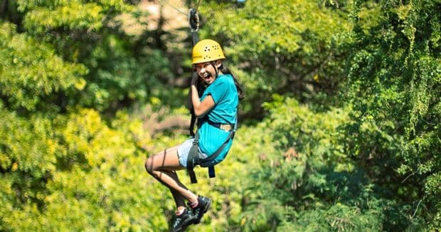 Girl in a yellow helmet laughing mid-ride on a Coral Crater zipline in Kapolei, Oʻahu
