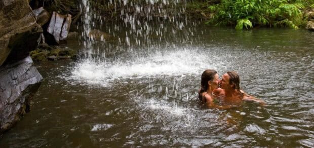 Two guests in the pool beneath a narrow waterfall in North Kohala