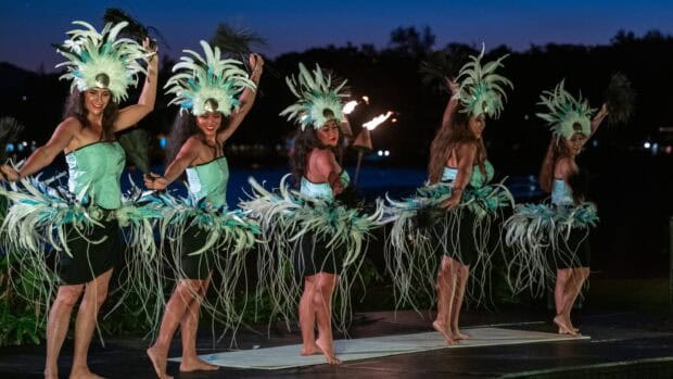 Five dancers in green feather headdresses and fringed skirts perform at dusk at the Royal Sonesta Kauaʻi lūʻau