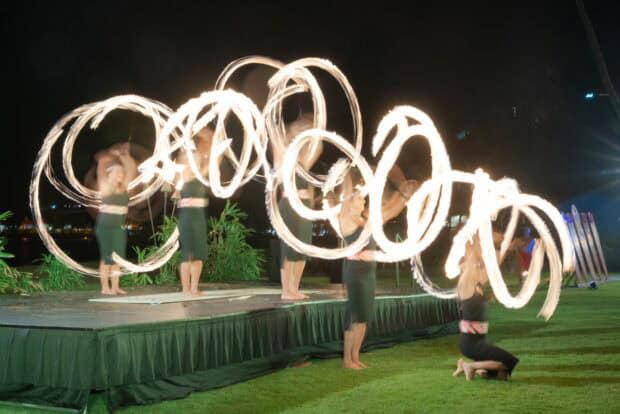 Dancers swing flaming poi balls in wide loops on the stage and lawn at the Royal Sonesta Kauaʻi lūʻau