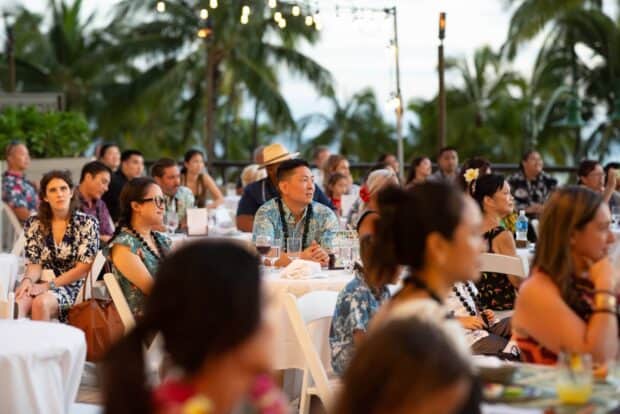 Guests seated at round tables on the open-air terrace with palms and string lights at dusk