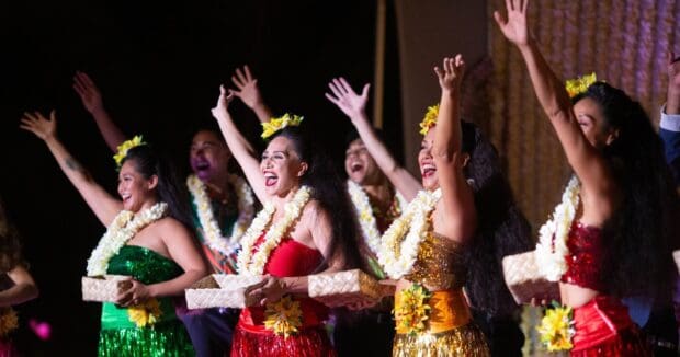 Dancers in green, red and gold raise their arms with woven baskets during the show finale