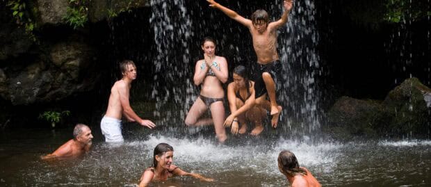 Group of guests swimming and jumping in under a waterfall in North Kohala