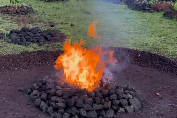 Fire burning inside a ring of lava rocks on bare ground at the Imu Mea ʻAi food tour near Pāhoa