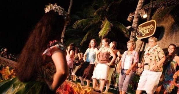 Guests on stage learning hula at Germaine's Luau, with a dancer in the foreground and the venue sign behind