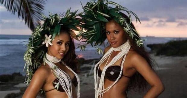 Two Germaine's Luau dancers in leaf headdresses and shell lei posed on the beach at sunset