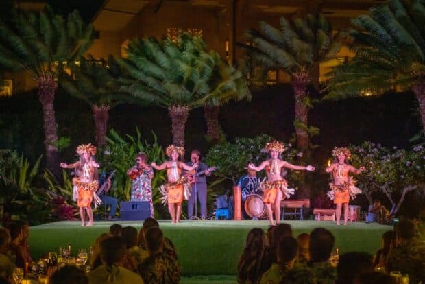 Four dancers in orange Tahitian costume perform in front of the live band at the Grand Hyatt Kauaʻi lūʻau