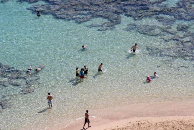 Snorkelers and families in shallow clear water over the inner reef flat at Hanauma Bay, seen from above