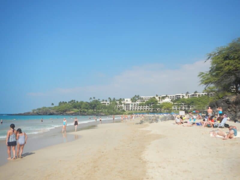 White sand and shallow surf at Hāpuna Beach, with the resort at the north end of the bay behind the palms