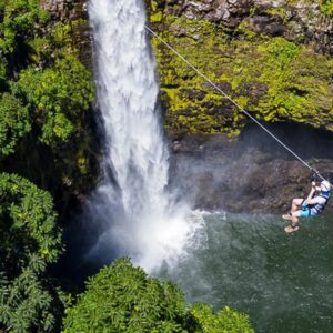 Zipliner crossing in front of a tall waterfall