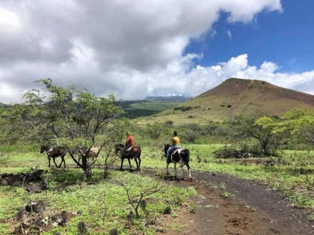 Horseback riders on a dirt track below a grassy cinder cone, Triple L Ranch, Maui