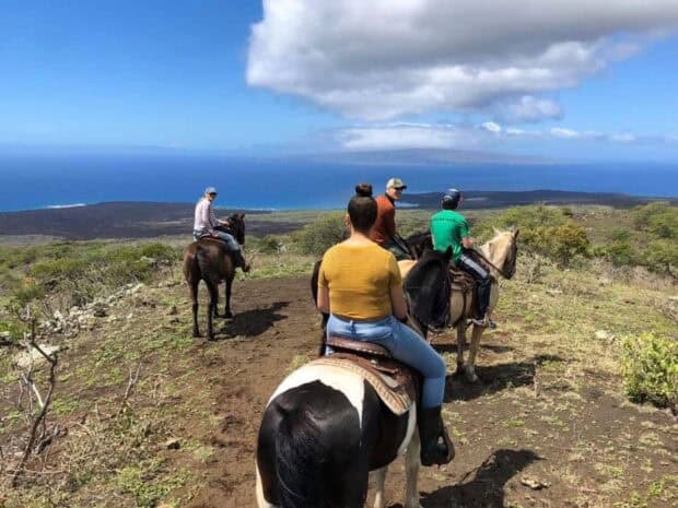 View from behind a rider on a paint horse as the group heads downhill toward the ocean and lava shoreline, Triple L Ranch