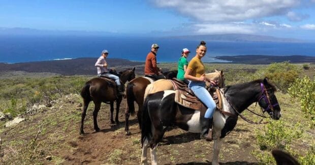 Four riders on horseback on a dirt trail above the ocean and a lava coastline, Triple L Ranch horseback ride, Maui
