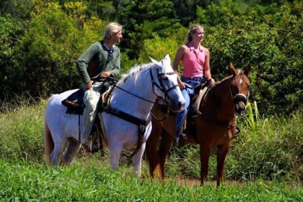 Two riders on a white horse and a chestnut horse on a grassy trail at Ironwood Ranch