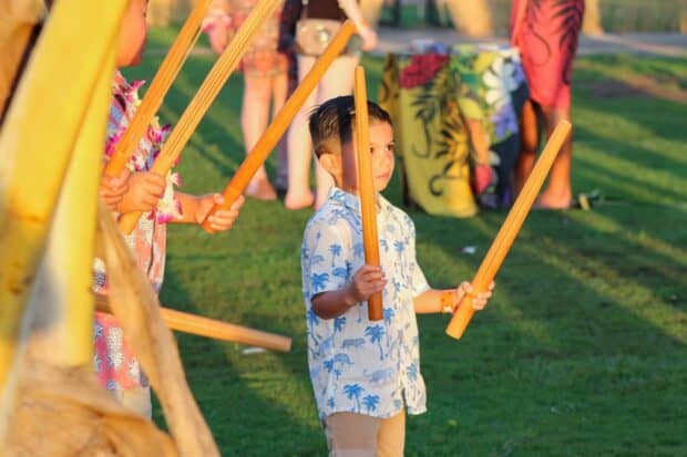 Young boy playing bamboo pipe instruments on the lawn during pre-show activities
