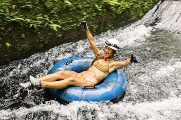A tuber in a helmet and headlamp floats a fern-lined irrigation canal on the Kauaʻi Backcountry mountain tubing tour