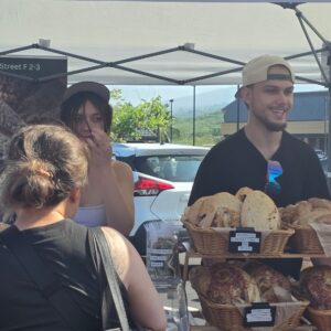 Arise Bakery vendor serving customers behind baskets of sourdough at the Keauhou Farmers Market