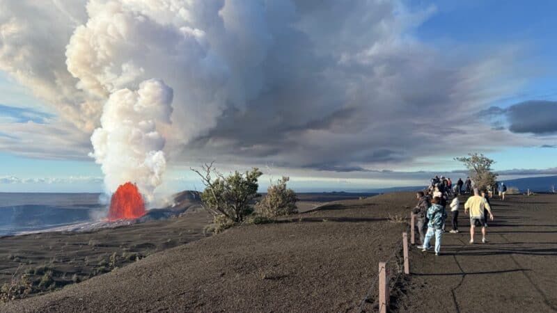 Visitors on the gravel trail at Uēkahuna overlook watching a Kīlauea lava fountain and its tall gas plume across the caldera